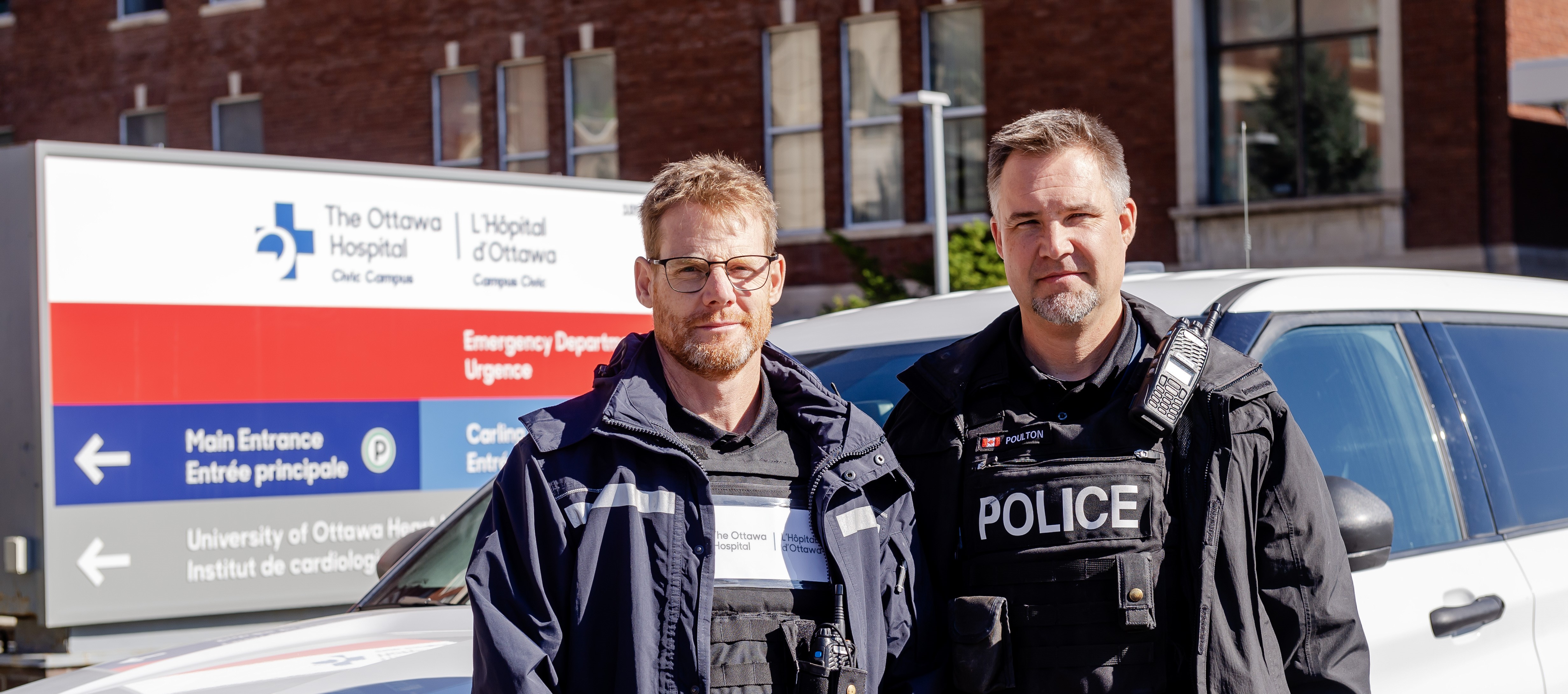 A photo of a Crisis Intervention Team member from the Ottawa Police standing with a member of the Ottawa Hospital in front of the Civic Hospital in Ottawa.