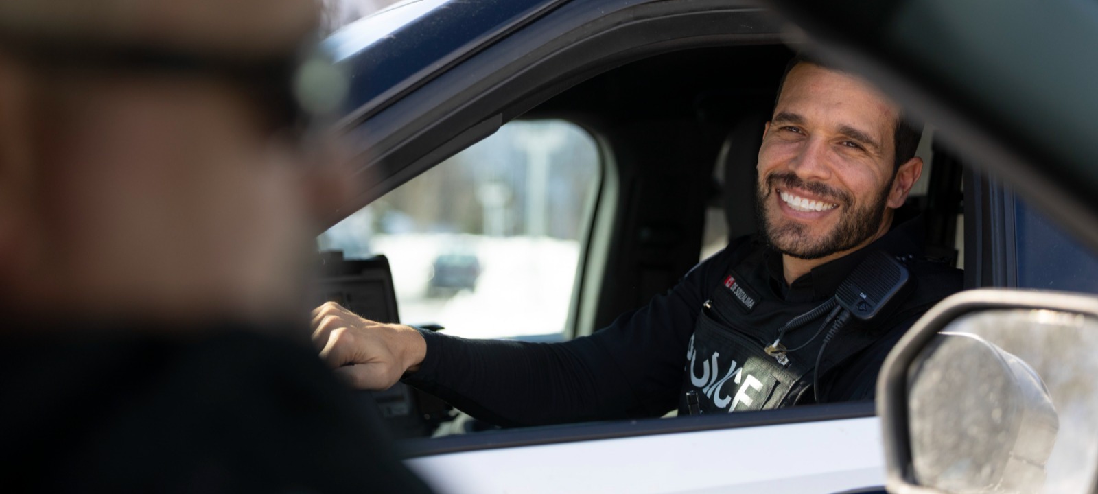Male police officer smiling in a police cruiser.