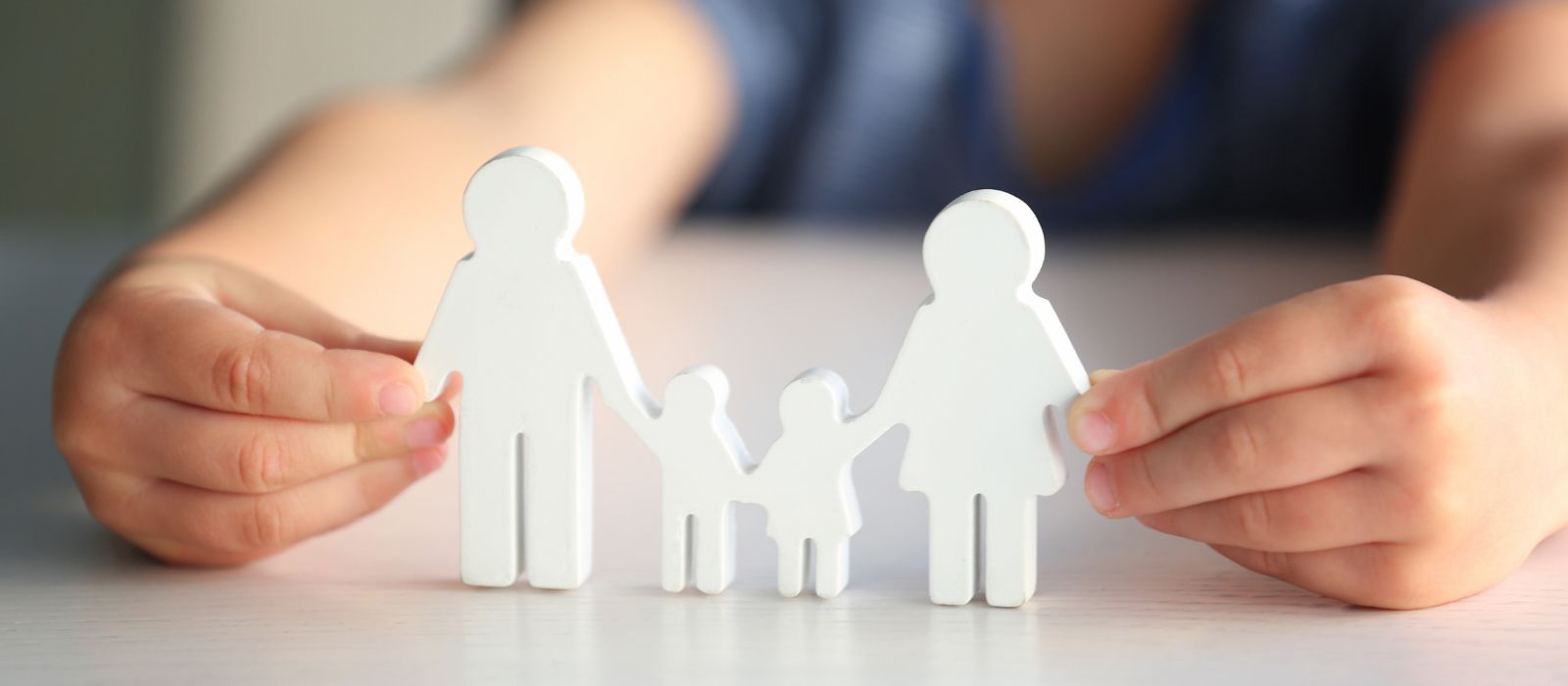 A child holds up a wooden cut of two parents and two children.