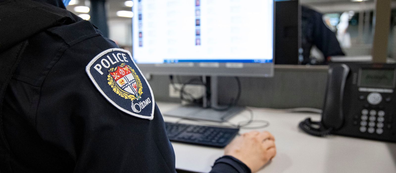 A police officer sitting at a desk in front of a computer. 