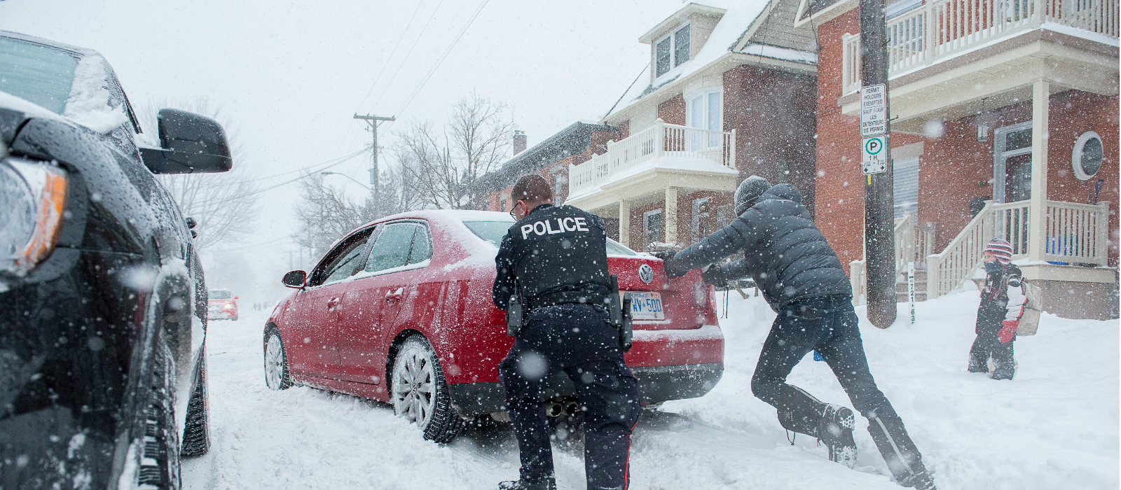 Un agent de la police communautaire aide un résident pendant une tempête hivernale en poussant sa voiture bloquée.