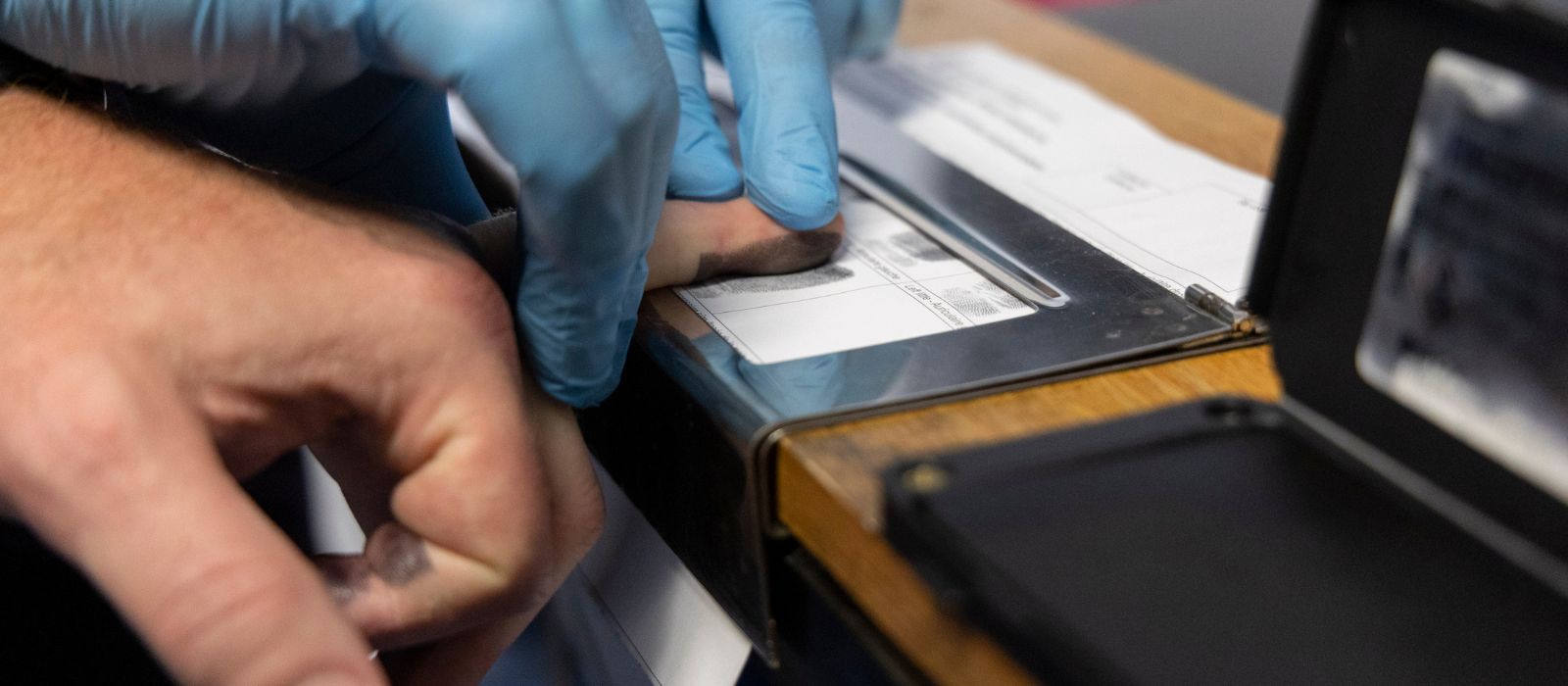 An individual having their finger dipped in ink for fingerprinting.