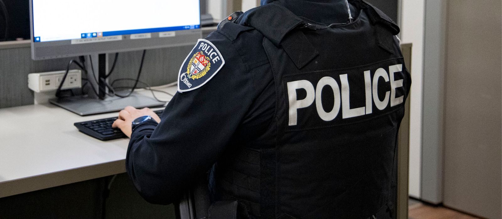 A police officer at a desk in front of a computer. 