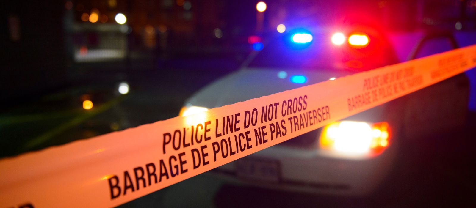 Police tape in front of a police cruiser at night.