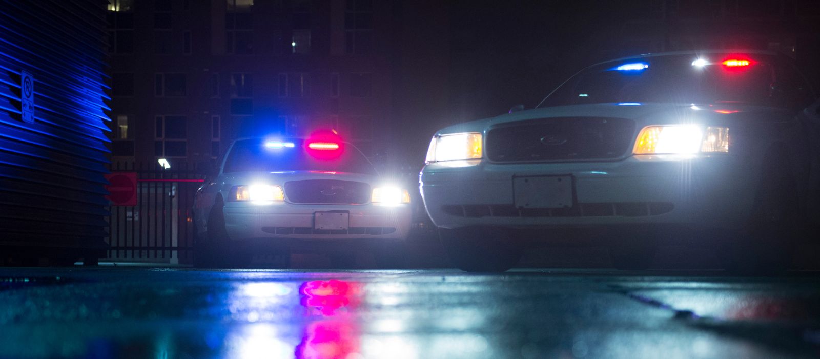 Two police cruisers with their lights on outside an apartment building at night.