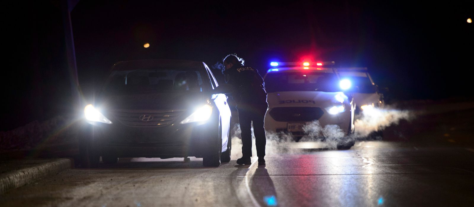 An Ottawa Police officer conversing with the driver of a vehicle they pulled over at night. 