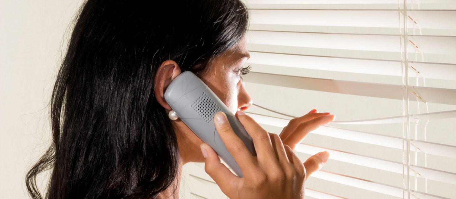 A concerned neighbour looks out her window while on the phone.