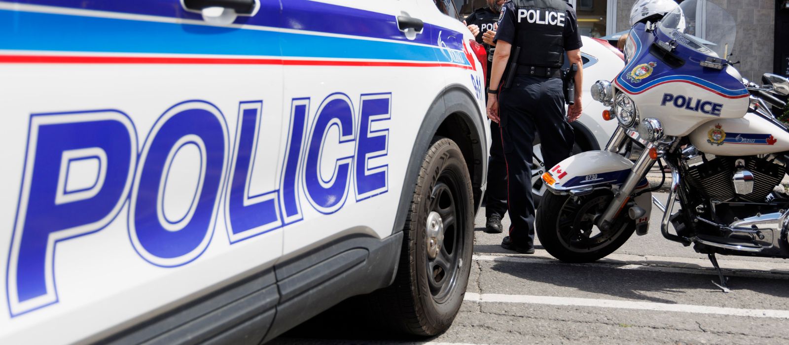 Two police officers standing between a police cruiser and motorcycle.