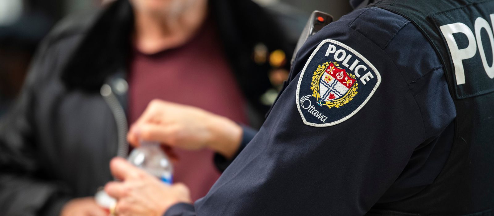 A police officer speaks with a member of the public holding a water bottle.