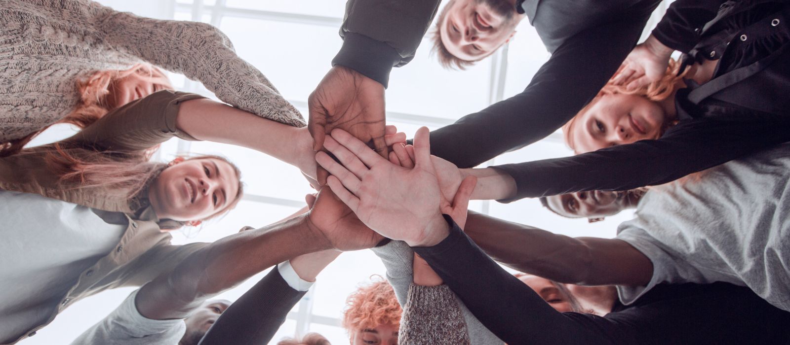 A group of youth standing in a circle with hands piled into the centre. 