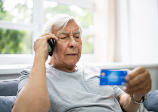 Fraud: elderly gentleman sitting in living room reading out his credit card information over the phone.