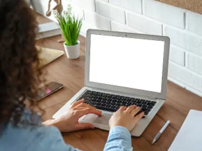 Woman working on a laptop at a desk. / Une femme travaillant sur un ordinateur portable à son bureau. 