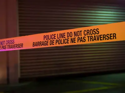 A storage locker with police tape in front of it at night. / Un casier de rangement devant lequel est tendu un ruban de police, la nuit.