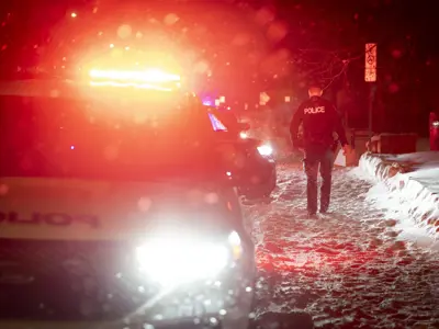 Police officer walking in the snow next to two police vehicles