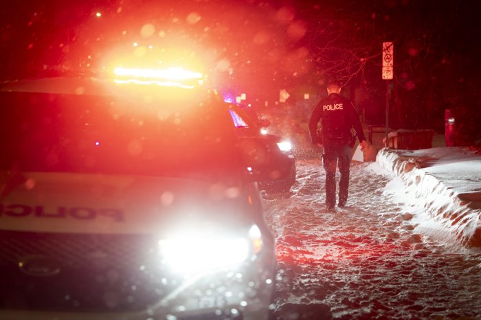Un agent de police marchant dans la neige à côté de deux véhicules de police